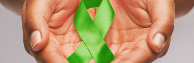 Duas mãos segurando um laço verde, da campanha Julho Verde.