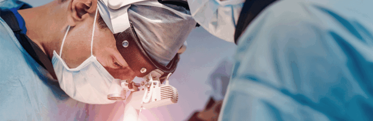 Médicos realizando procedimento cirúrgico, olhando para baixo.