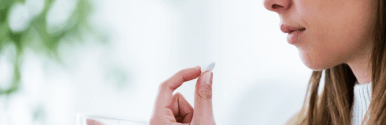 Mulher segurando um copo d'água e se medicando.